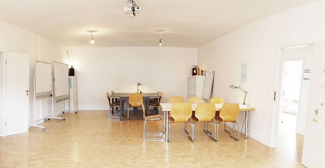 Foto eines buchbaren Raums des Vereins wasmitherz in Hannovers Nordstadt. Zu sehen ist ein größerer Raum mit mobiler Bestuhlung, Tischen, einem Beamer, Pinwänden und Flipchart.
